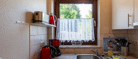 Una cocina pequeña con ventana, un lavamanos y varios electrodomésticos.