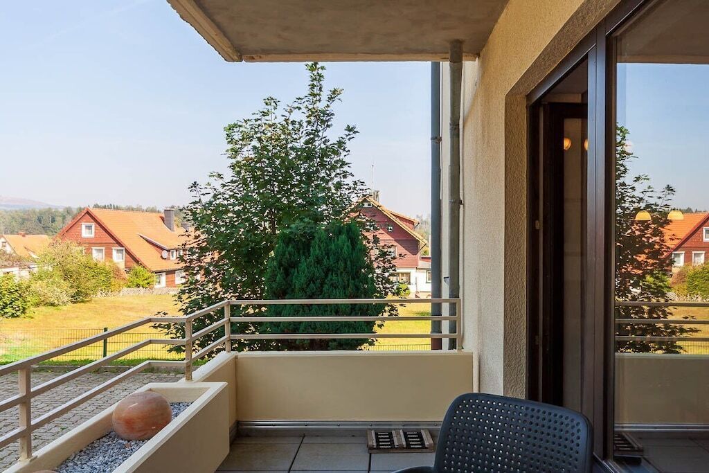 A balcony with a chair, a potted plant, and a view of houses and trees.