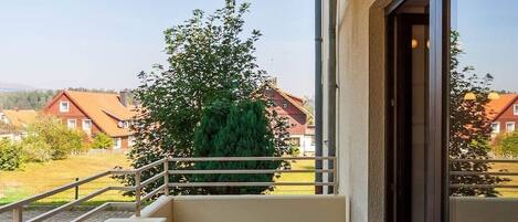 A balcony with a chair, a potted plant, and a view of houses and trees.