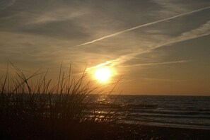 Ein Sonnenuntergang über dem Ozean bei klarem Himmel und einem sichtbaren Kondensstreifen.
