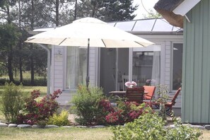 Eine überdachte Terrasse mit Gartenmöbeln, umgeben von einem Garten mit verschiedenen Pflanzen und Blumen.