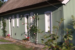 Ein grünes Gebäude mit einem Strohdach, weißen Fenstern und einem kleinen Garten mit rosa Blumen.