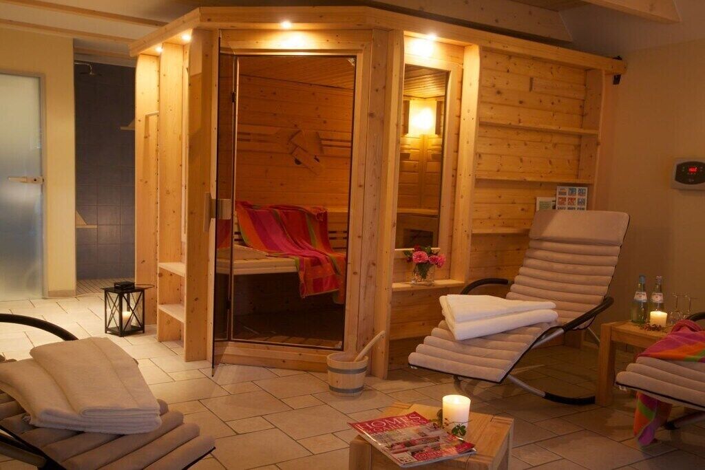 Ein Saunaraum mit Holzboden, Glastür, Massagesessel und einem kleinen Tisch mit Kerze und Zeitschrift.