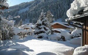 Schneebedeckte Landschaft mit einer Holzhütte und einem mit Schnee beladenen Baum im Vordergrund.