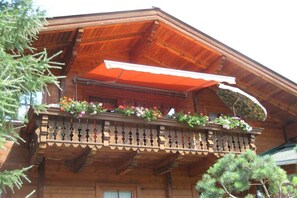 Ein Holzhaus mit Balkon, geschmückt mit Blumen, und einem hängenden Sonnenschirm.