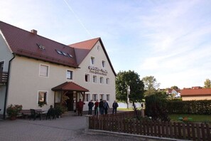 A building with a sign indicating it's a guesthouse, a paved entrance, and a small outdoor seating area. - Carp House - Courtyard Pond (Feuchtwangen)
