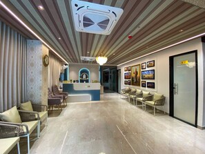A hotel reception area with a modern design, featuring a reception desk, seating area, and a hallway leading to other rooms. - Hotel JJM Palace (Udaipur)