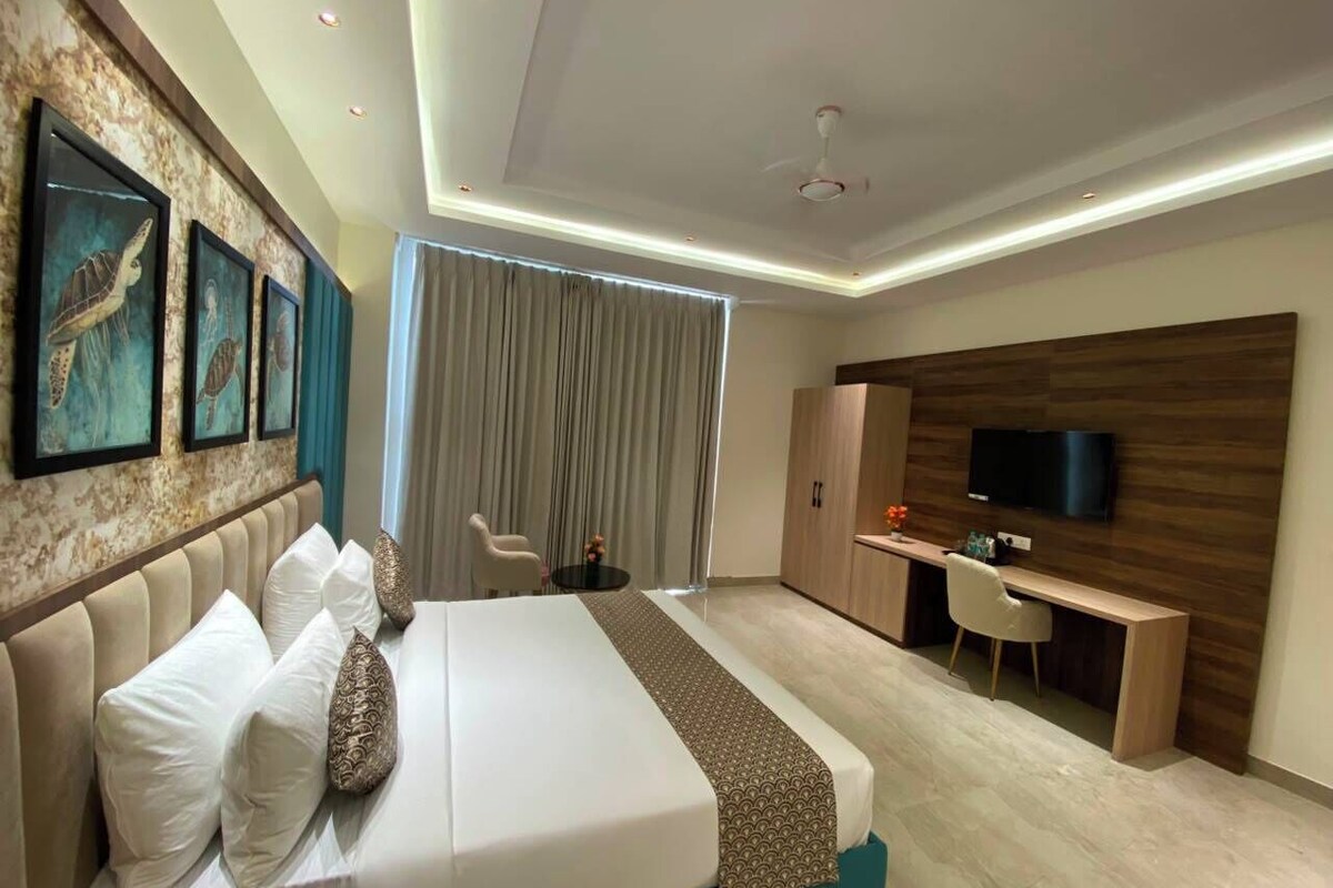 A modern hotel room with a large bed, a desk, a television, and a view of the city.