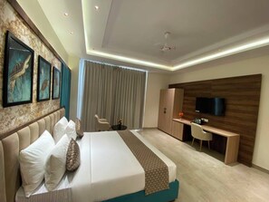 A modern hotel room with a large bed, a desk, a television, and a view of the city. - Hotel JJM Palace (Udaipur)