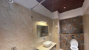 Ein modernes Badezimmer mit einer gläsernen Duschkabine, einem weißen Waschbecken und einer Toilette mit Fliesenspiegel.