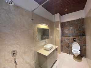 A modern bathroom with a glass-enclosed shower, a white sink, and a toilet with a patterned tile backsplash. - Hotel JJM Palace (Udaipur)
