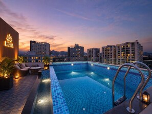 A rooftop swimming pool with a view of surrounding buildings at dusk. - Hotel JJM Palace (Udaipur)