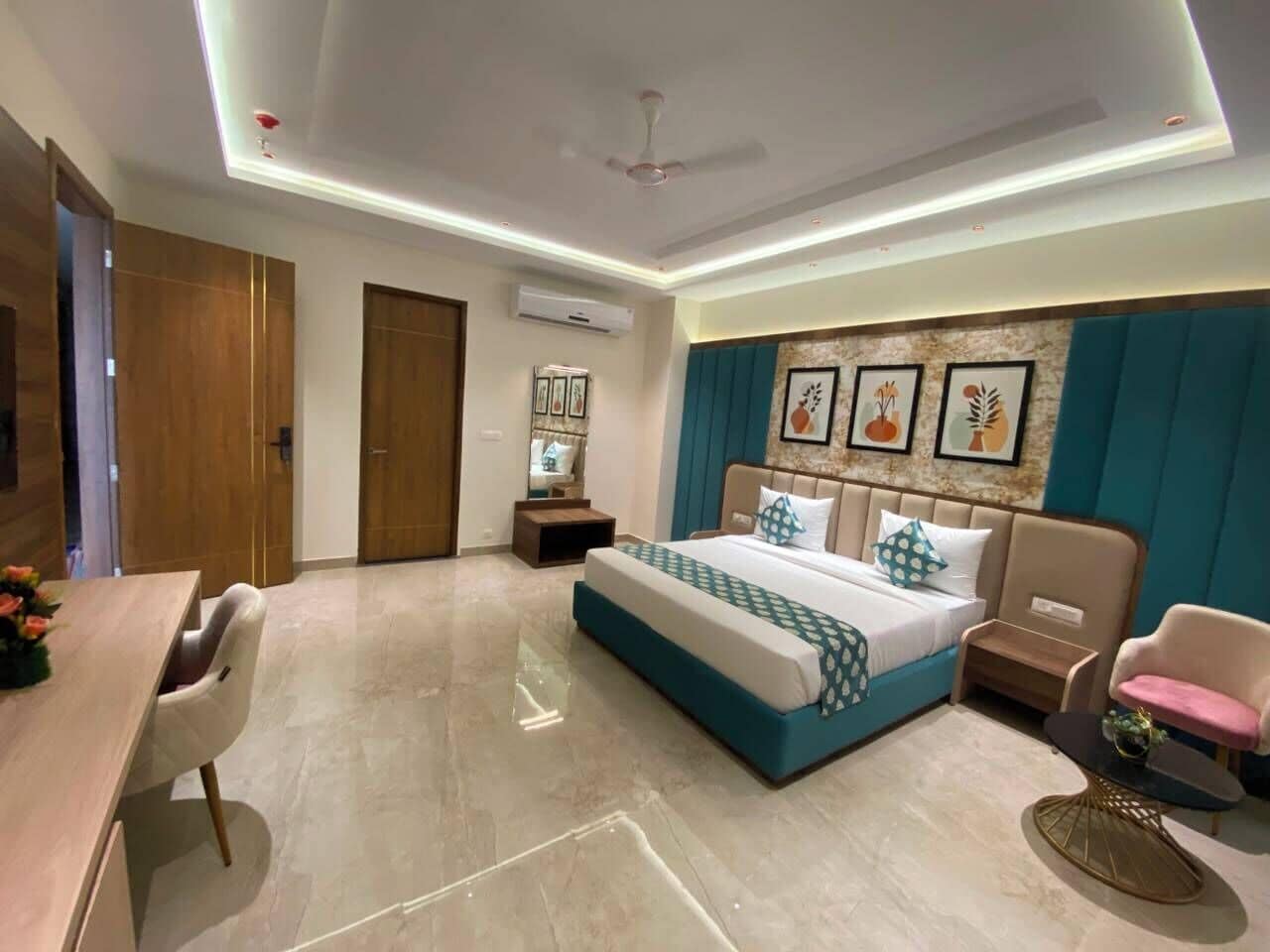 Quarto de hotel com cama, escrivaninha, cadeira, mesinha e ventoinha no teto.
