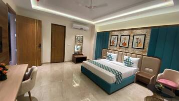 Quarto de hotel com cama, escrivaninha, cadeira, mesinha e ventoinha no teto.