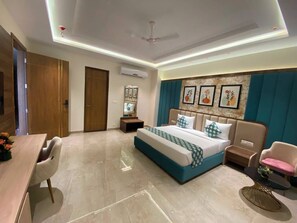Una habitación de hotel con una cama, un escritorio, una silla, una mesita pequeña y un ventilador de techo.