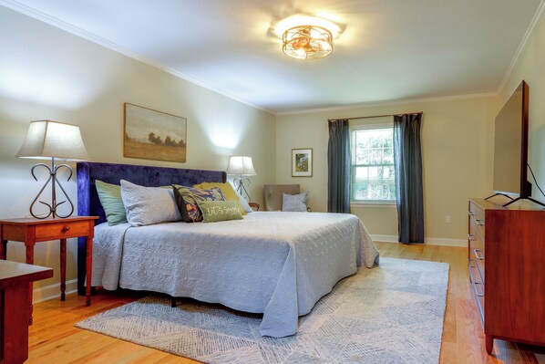 A bedroom with a bed, two bedside tables, a dresser, a window with curtains, and a ceiling light fixture.