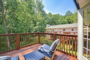 A wooden deck with outdoor furniture, a view of a house, and a forested area.