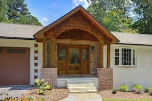 A two-story house with a front porch, a garage, and a small garden area with mulch and plants.