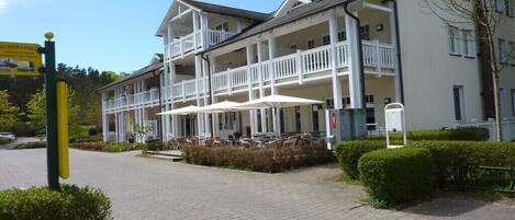 A hotel with a covered outdoor seating area, multiple balconies, and a paved entrance.