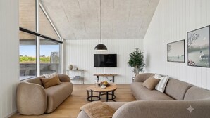 A modern living room with two sofas, a coffee table, a TV, and a large window offering a view of greenery. - VillaVilla 972 - Ålbæk, Nordjylland (Ålbæk)