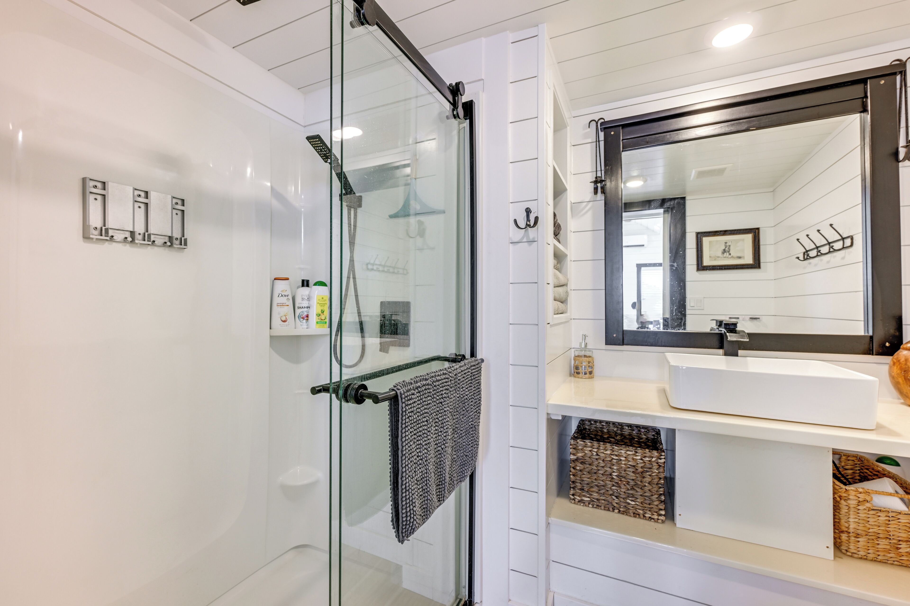 Un baño moderno con cabina de ducha de vidrio, lavamanos blanco y un espejo grande.