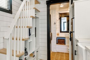 A staircase with white railings and wooden steps leading to a room with a white door, a mirror, and a refrigerator. - Gateway to Red Rock Adventures! Resort Tiny Home (Apple Valley)
