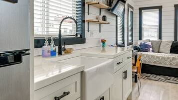 A compact kitchenette with a sink, storage cabinets, and a window with blinds.
