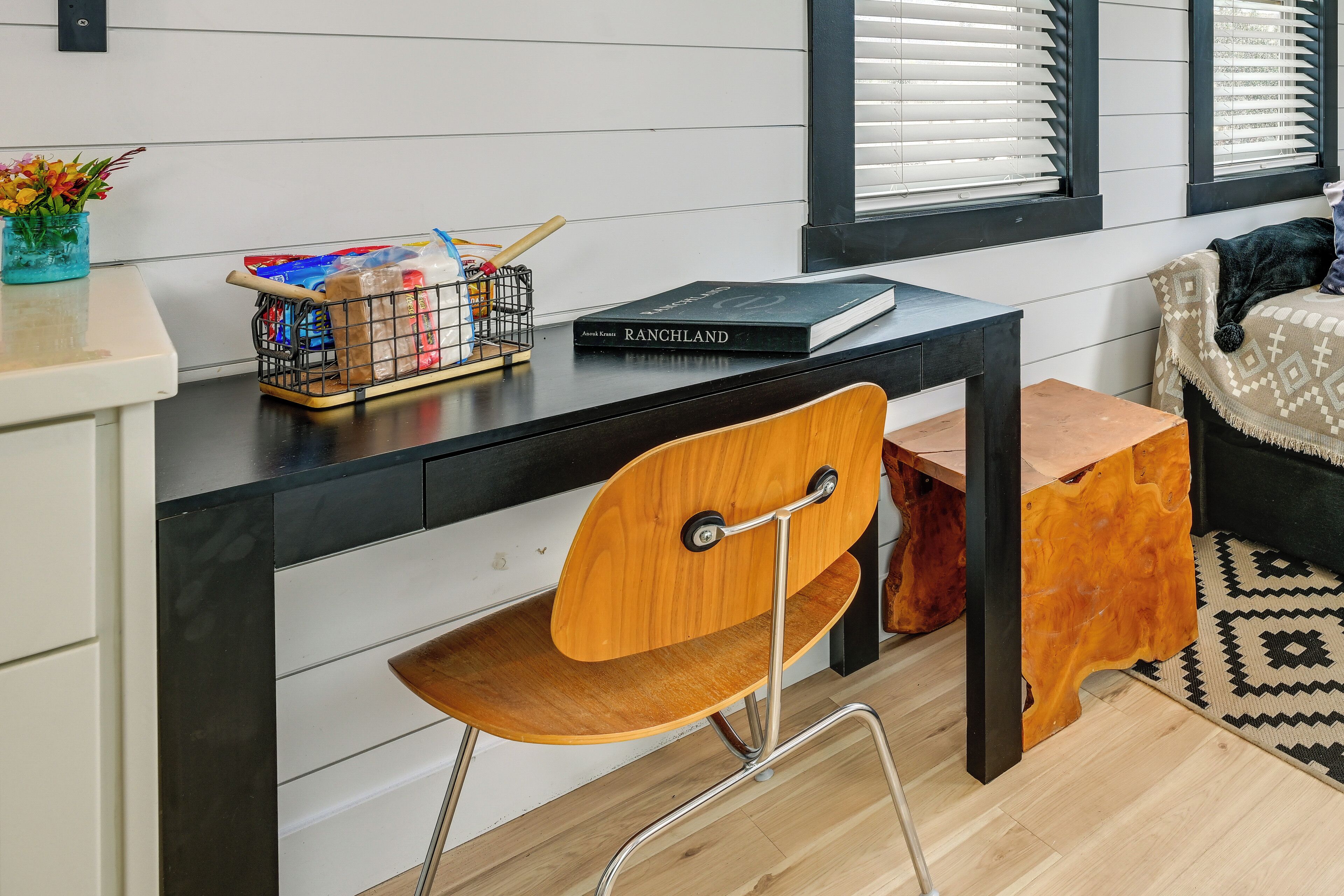 A modern room with a black desk, a wooden chair, a small wooden stool, and a patterned rug.