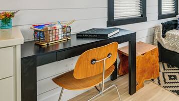 A modern room with a black desk, a wooden chair, a small wooden stool, and a patterned rug.
