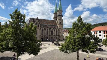 Eine historische Kirche mit einem markanten Turm und einem gepflasterten Platz mit Bänken und Bäumen.
