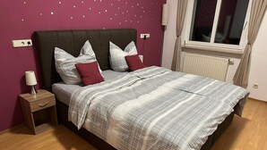 Un dormitorio con cama, mesita de noche, lámpara y ventana con cortinas.