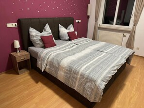 Een slaapkamer met een bed, nachtkastje, lamp en een raam met gordijnen.