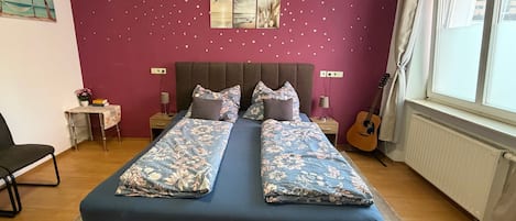 Une chambre à coucher avec un lit double, une petite table avec une lampe, une guitare et une fenêtre avec des rideaux.