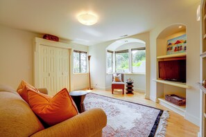 A well-lit living room with a sofa, a patterned rug, and a television on a shelf.