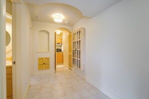 A hallway with a kitchen area, a door with a small window, and a light fixture on the ceiling.