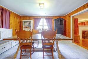 A dining area with a wooden table and chairs, a bookshelf, and a view through a window.