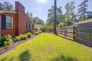 A backyard with a brick house, a wooden fence, and a grassy lawn.