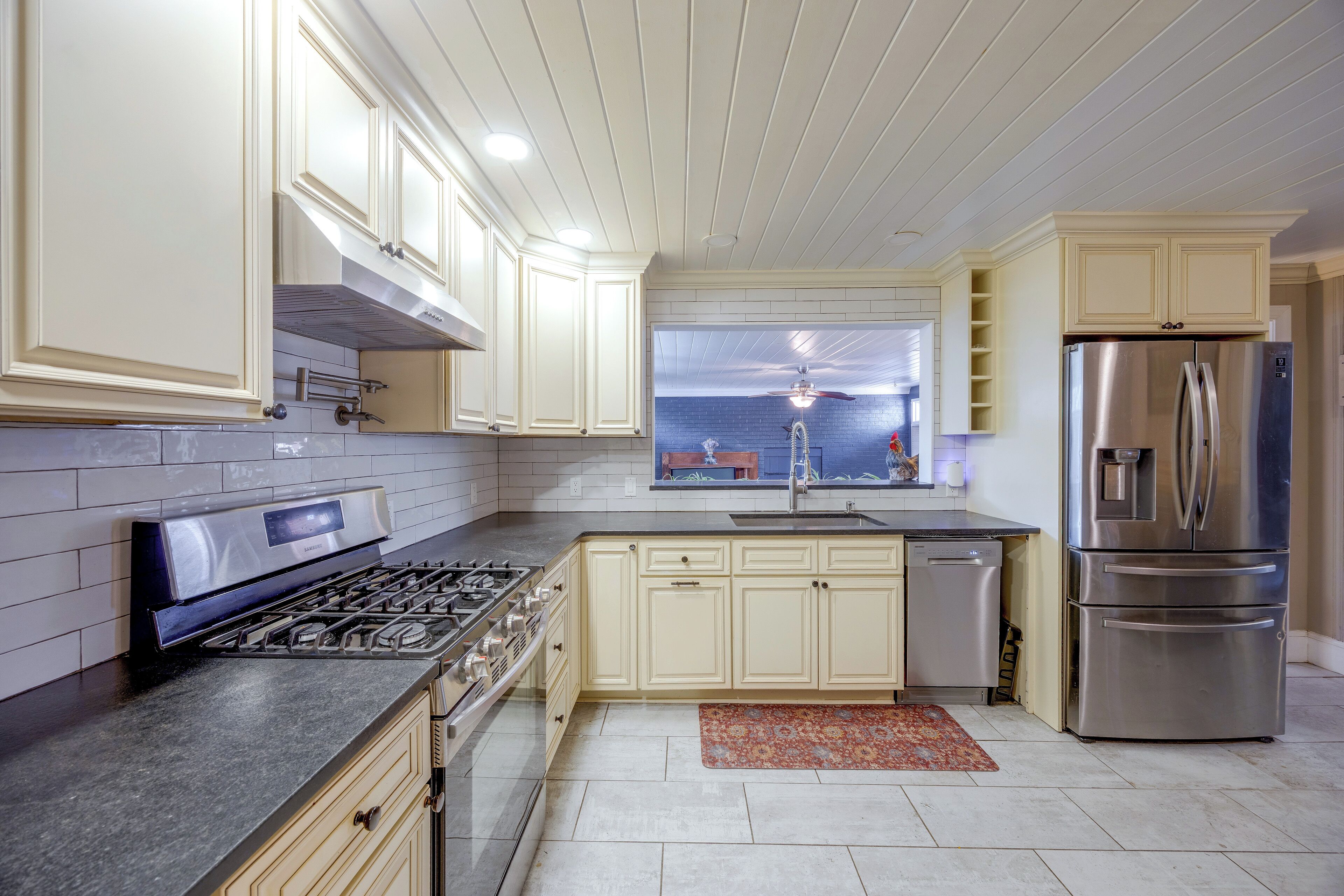 A modern kitchen with white cabinetry, a stainless steel refrigerator, a gas stove, and a window above the sink.