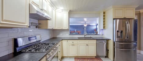 A modern kitchen with white cabinetry, a stainless steel refrigerator, a gas stove, and a window above the sink.
