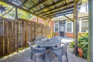 Une terrasse couverte avec une table ronde et des chaises, une clôture en bois et une maison en briques en arrière-plan.