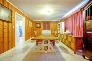 Une salle à manger avec une longue table en bois, des chaises, un buffet et une porte donnant sur une autre pièce.