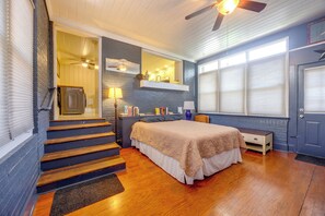 Une chambre à coucher comprenant un lit, une table de chevet, une commode, une fenêtre avec des stores, un ventilateur de plafond et un escalier.