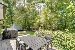 Una veranda esterna con tavolo e sedie, circondata da un giardino con alberi e un capanno.