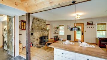 A spacious kitchen with a stone fireplace, wooden beams, and a dining area with a table set for two.