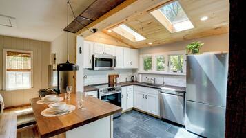 A modern kitchen with white cabinets, stainless steel appliances, a wooden countertop, and a skylight.
