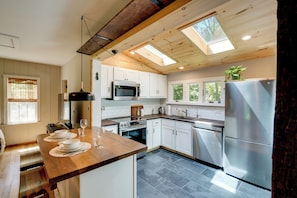 A modern kitchen with white cabinets, stainless steel appliances, a wooden countertop, and a skylight.