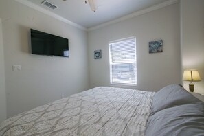 A bedroom with a bed, a television mounted on the wall, a window with blinds, and a small table with a lamp. - Private Dock, Pool Access:  Oceanfront Cottage (Port Isabel)