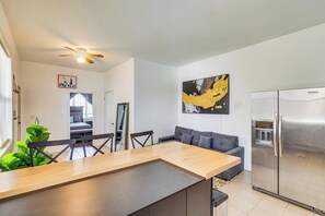 Eine moderne Küche mit einem Edelstahlkühlschrank, einem Essbereich mit Holztisch und -stühlen, einem grauen Sofa und einem Deckenventilator.