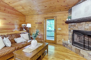 A wooden interior with a leather sofa, a stone fireplace, and a door leading outside. - Hot Tub Haven! Family-Friendly Blue Ridge Cabin (Blue Ridge)