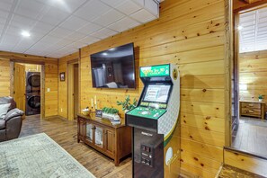 A room with wooden walls, a flat-screen TV mounted on the wall, a console table with a plant, a sofa, and a washing machine. - Hot Tub Haven! Family-Friendly Blue Ridge Cabin (Blue Ridge)